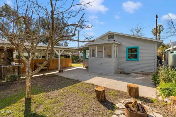 a backyard of a house with table and chairs potted plants and a large tree