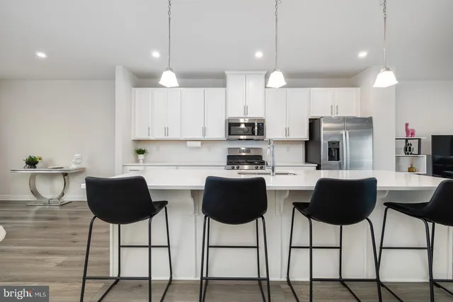 a kitchen with stainless steel appliances a refrigerator a stove top oven a sink dishwasher and a dining table with wooden floor