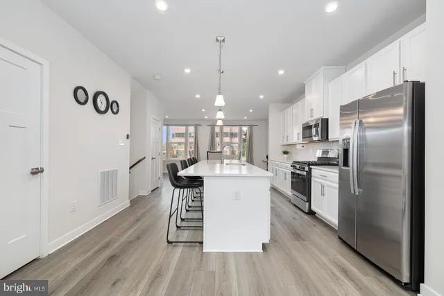 a kitchen with stainless steel appliances kitchen island granite countertop a refrigerator a stove a sink dishwasher and a dining table with wooden floor