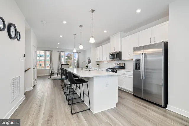 a kitchen with stainless steel appliances kitchen island granite countertop a stove a sink a refrigerator and white cabinets with wooden floor