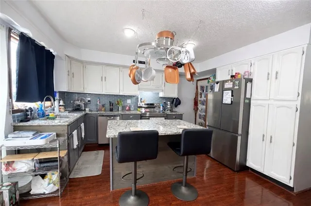 a kitchen with stainless steel appliances granite countertop a refrigerator a stove a sink dishwasher and a dining table with wooden floor