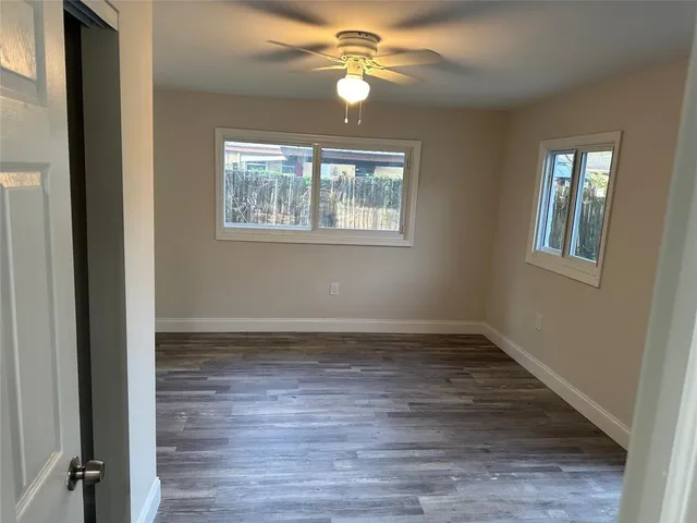 an empty room with wooden floor chandelier fan and windows