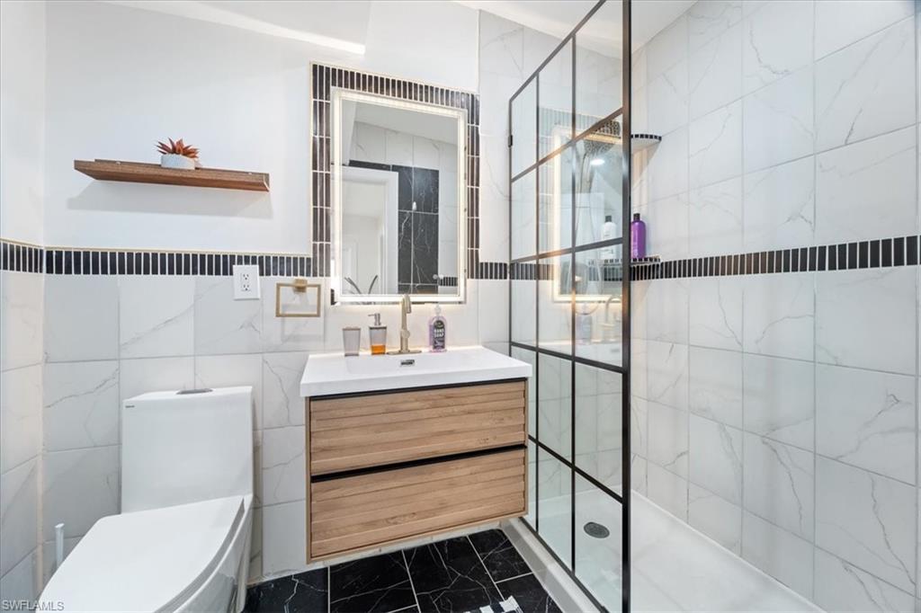 2123 Holiday Lane Naples, FL 34104 - Photo 10 of 32 Bathroom with toilet, a tile shower, tile walls, and vanity