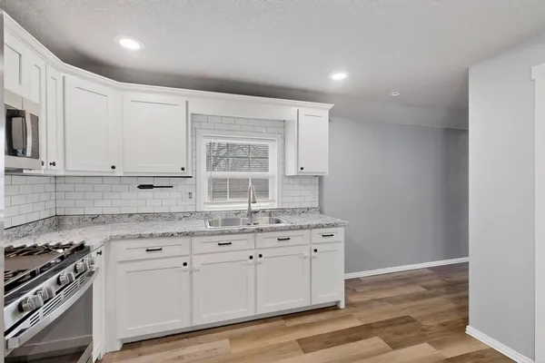 a kitchen with granite countertop a stove a sink and white cabinets