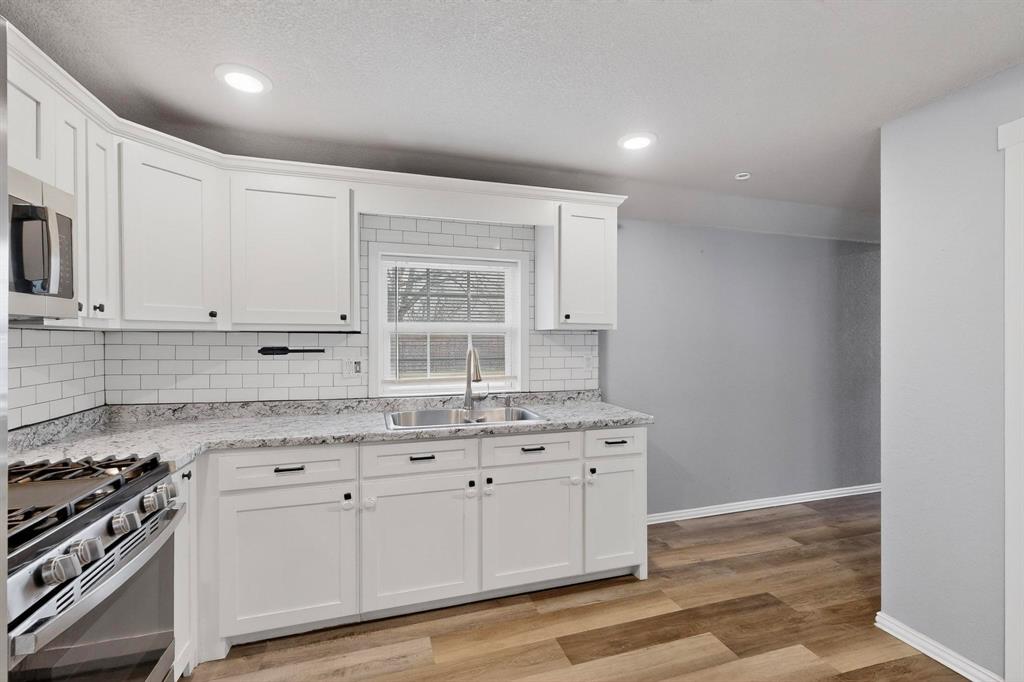 400 South Oak Street Ranger, TX 76470 - Photo 17 of 38 a kitchen with granite countertop a stove a sink and white cabinets