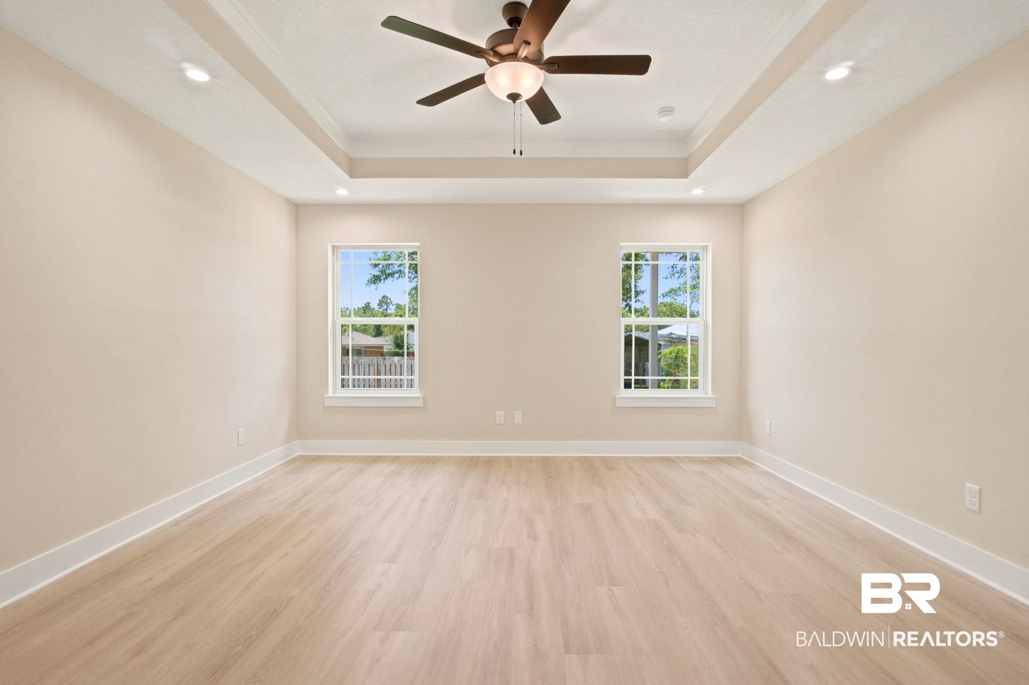 32656 Arbor Ridge Circle Lillian, AL 36549 - Photo 14 of 56 Spacious interior featuring two large windows, light wood-finish flooring, a contemporary ceiling fan, recessed lighting, and a tray ceiling with crown molding