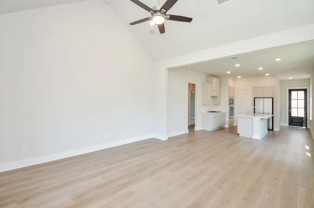 a view of a livingroom with a ceiling fan & kitchen space