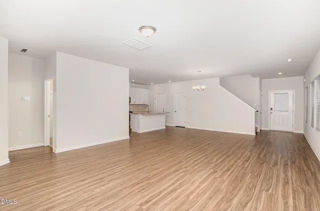 a view of an empty room with wooden floor and a kitchen