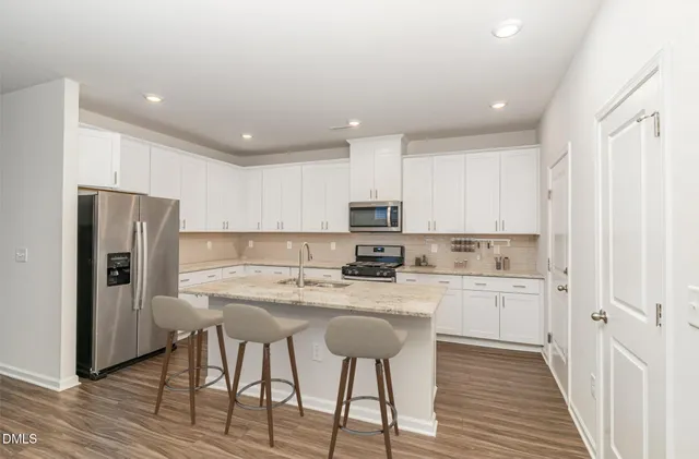 a kitchen with stainless steel appliances granite countertop a refrigerator a stove top oven a sink and white cabinets with wooden floor