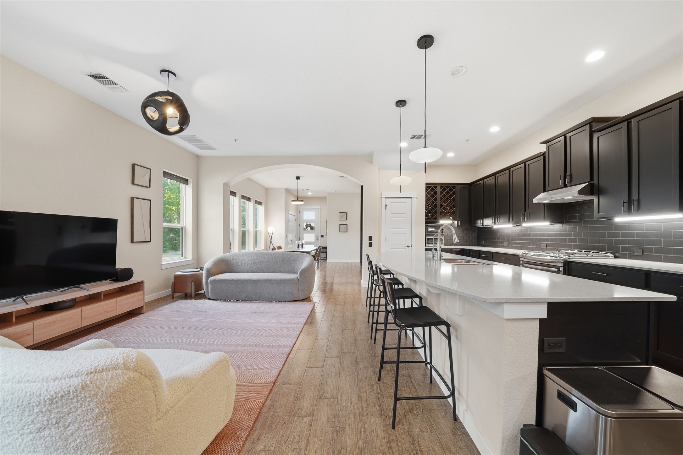 3901 Vaughan Street Austin, TX 78723 - Photo 12 of 37 Open-concept living area featuring wood-finish flooring, a kitchen island with seating, dark cabinetry, light countertops, and archways leading to additional spaces