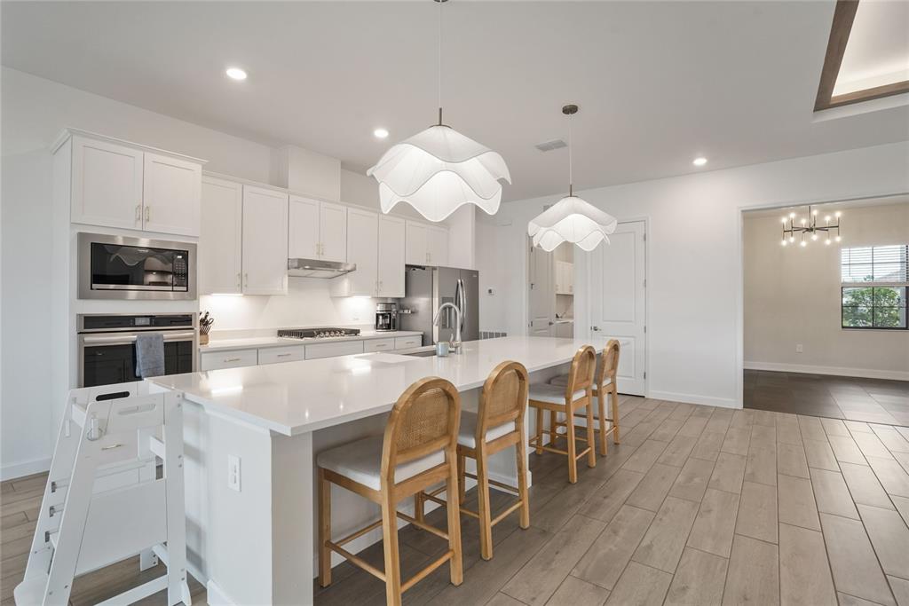 15906 Tradewind Terrace Lakewood Ranch, FL 34211 - Photo 8 of 67 a kitchen with stainless steel appliances granite countertop a stove top oven a sink dishwasher a dining table and chairs with wooden floor