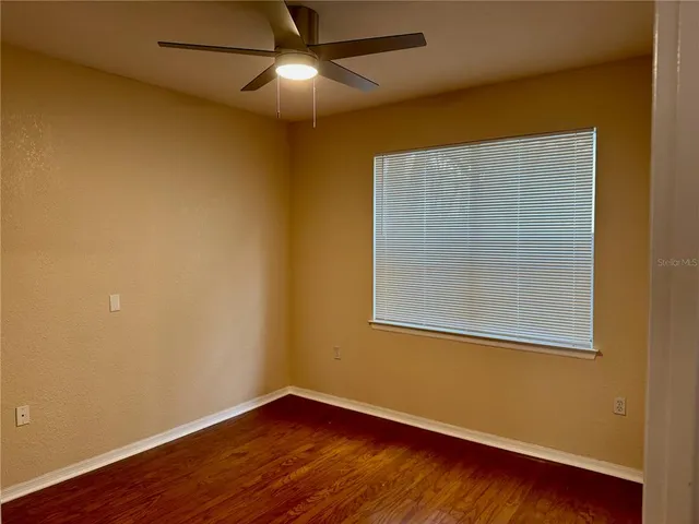 a view of empty room with wooden floor and fan