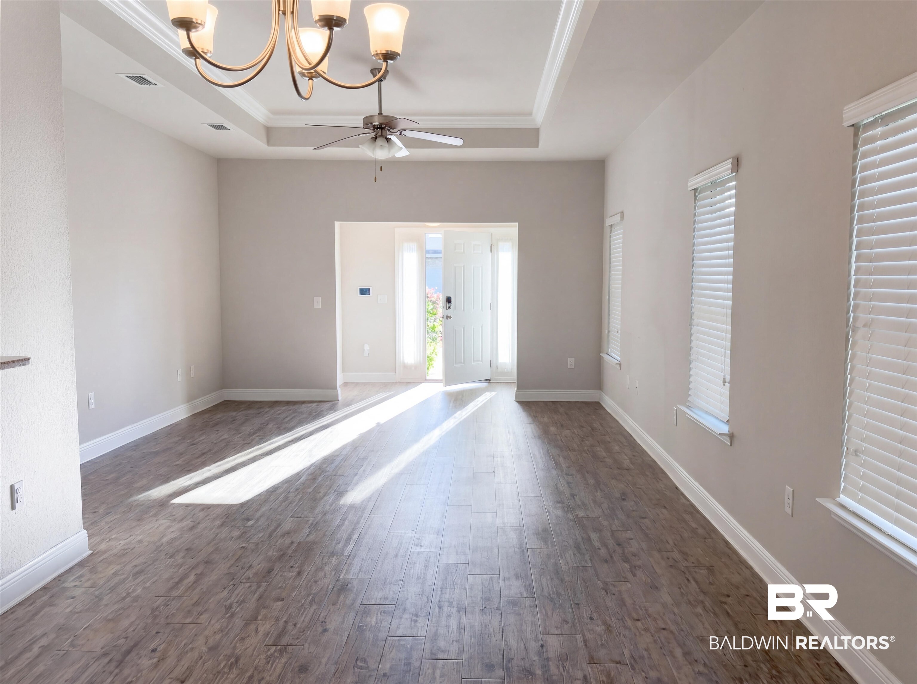 1740 Covington Lane Foley, AL 36535 - Photo 8 of 18 Spacious living area featuring wood-finish plank flooring, tray ceilings with crown molding, recessed lighting, and a prominent chandelier with an integrated ceiling fan