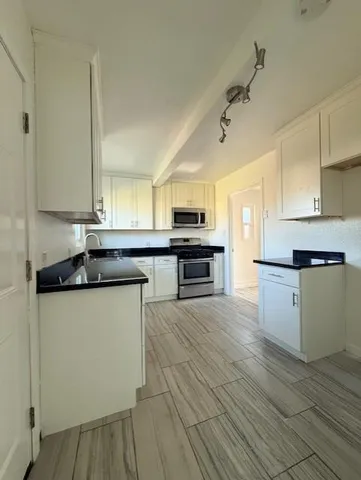 a large kitchen with granite countertop a stove top oven a sink dishwasher and white cabinets