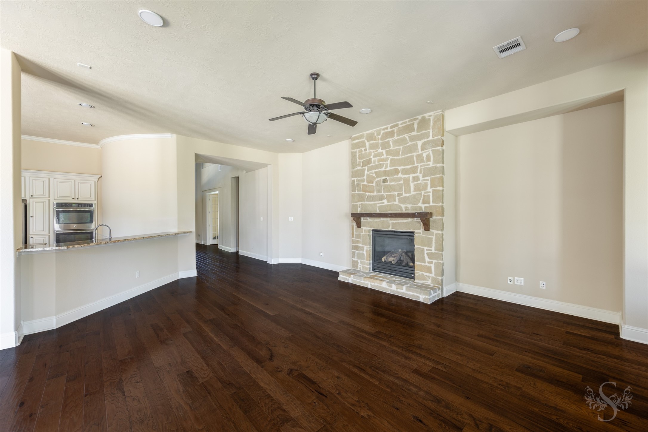 5803 Mustang Ridge Lane Fulshear, TX 77441 - Photo 11 of 48 Spacious family room showcases rich wood flooring, a floor-to-ceiling stone fireplace and an open-concept layout designed for gathering and entertaining. Expansive sightlines into the kitchen and breakfast area create a seamless flow throughout the main living spaces.