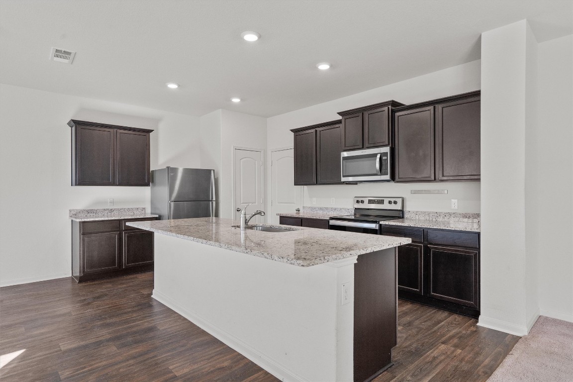 14405 Boomtown Way Elgin, TX 78621 - Photo 7 of 39 a kitchen with stainless steel appliances granite countertop a stove top oven a sink dishwasher a refrigerator and a microwave oven with wooden floor