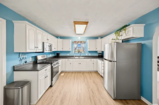 a kitchen with stainless steel appliances granite countertop a refrigerator a stove a sink dishwasher and white cabinets with wooden floor