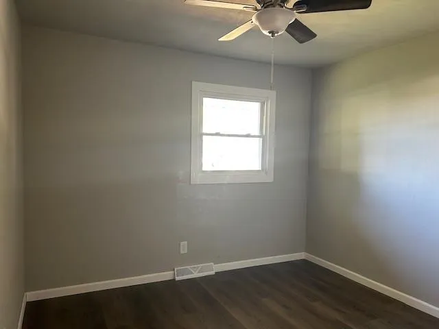 an empty room with wooden floor fan and windows