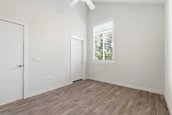 an empty room with wooden floor chandelier fan and windows
