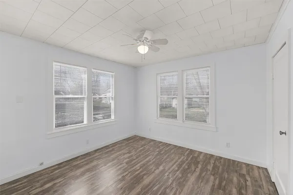 an empty room with wooden floor fan and windows