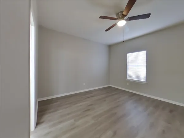an empty room with wooden floor ceiling fan and windows