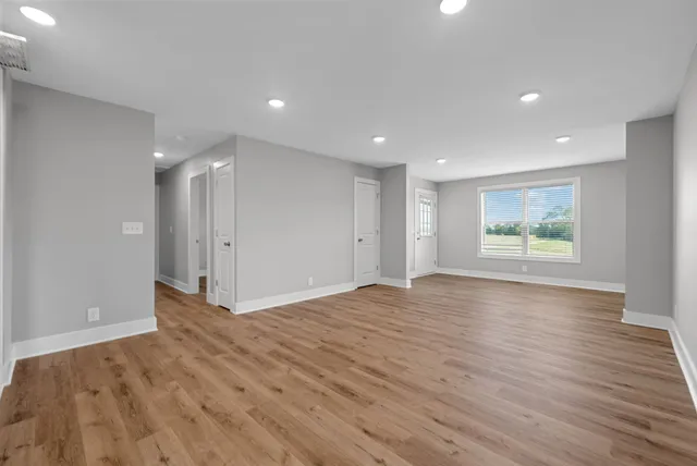 a view of an empty room with wooden floor and window