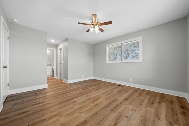 an empty room with wooden floor ceiling fan and windows