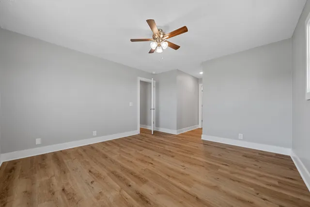 a view of an empty room with wooden floor and a ceiling fan