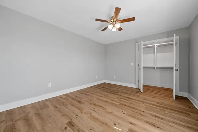 an empty room with wooden floor fan and windows