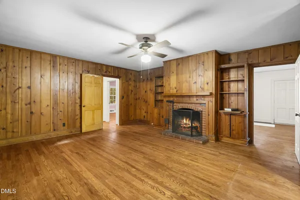 an empty room with windows fireplace and a kitchen view