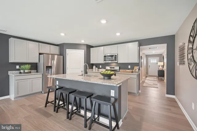 a kitchen with stainless steel appliances a refrigerator a stove top oven a sink dishwasher and white cabinets with wooden floor