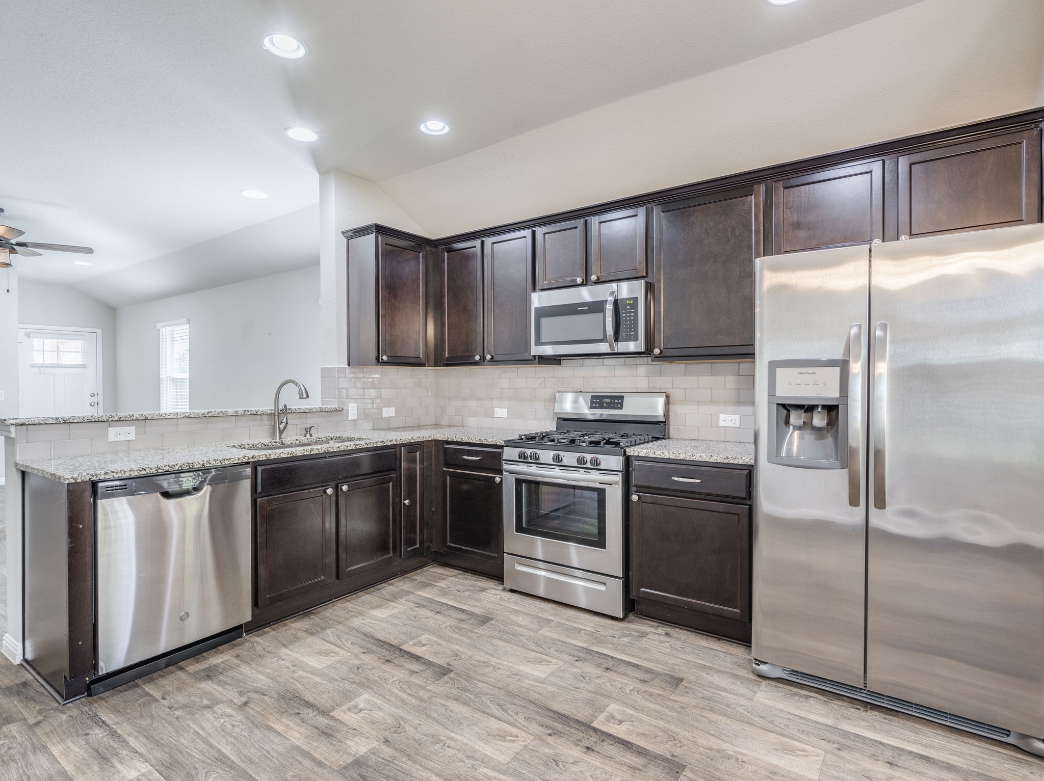 136 Dunlin Lane Leander, TX 78641 - Photo 8 of 24 Kitchen with stainless steel appliances, dark wood finish cabinetry, vaulted ceiling, light stone countertops, and light wood-type flooring