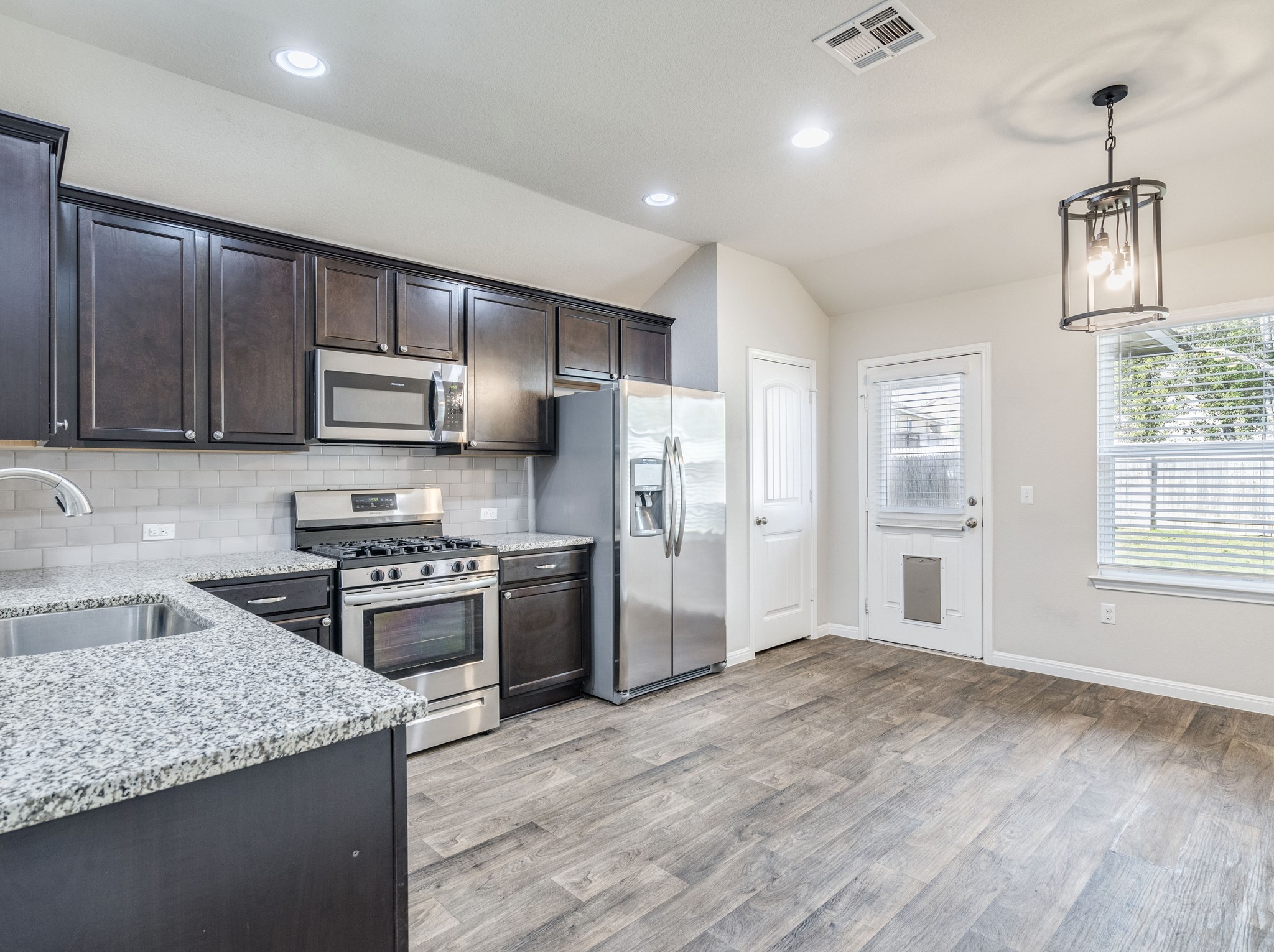 136 Dunlin Lane Leander, TX 78641 - Photo 9 of 24 Kitchen with light stone counters, stainless steel appliances, dark wood finish cabinets, vaulted ceiling, and tasteful backsplash