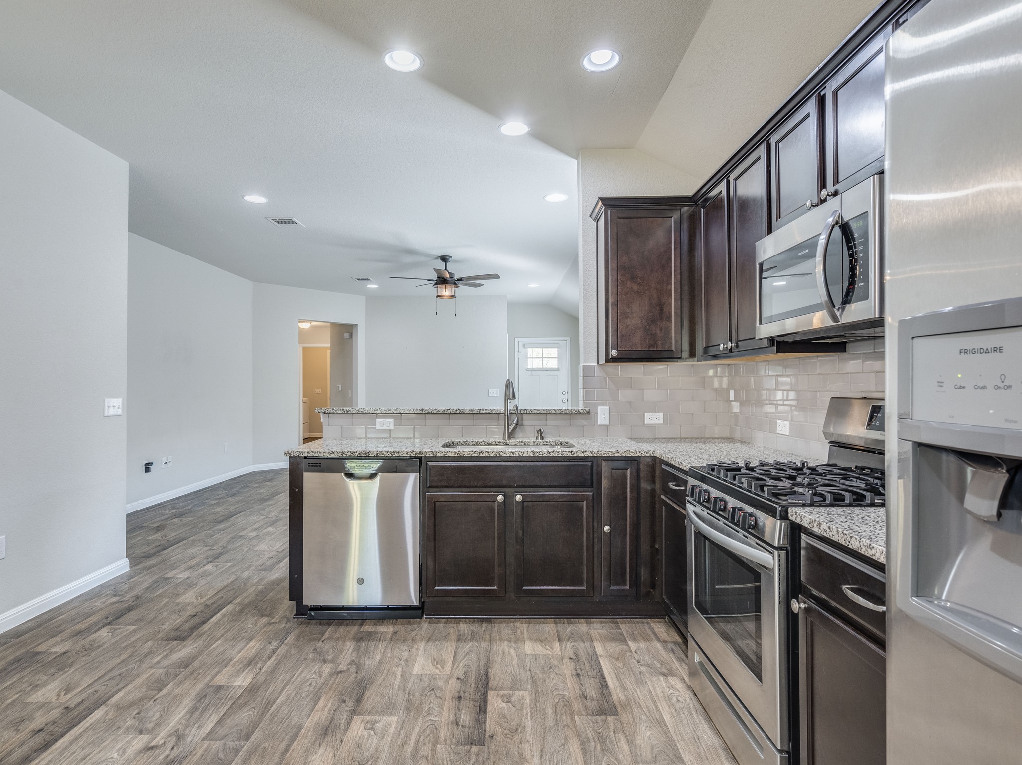 136 Dunlin Lane Leander, TX 78641 - Photo 10 of 24 Kitchen featuring stainless steel appliances, lofted ceiling, dark wood finish cabinetry, light stone counters, and a peninsula