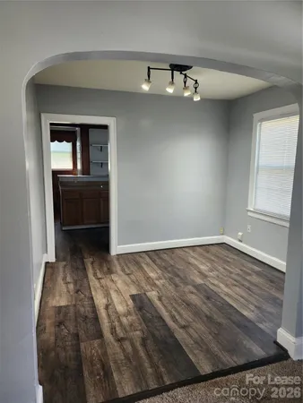 a view of empty room with wooden floor and kitchen