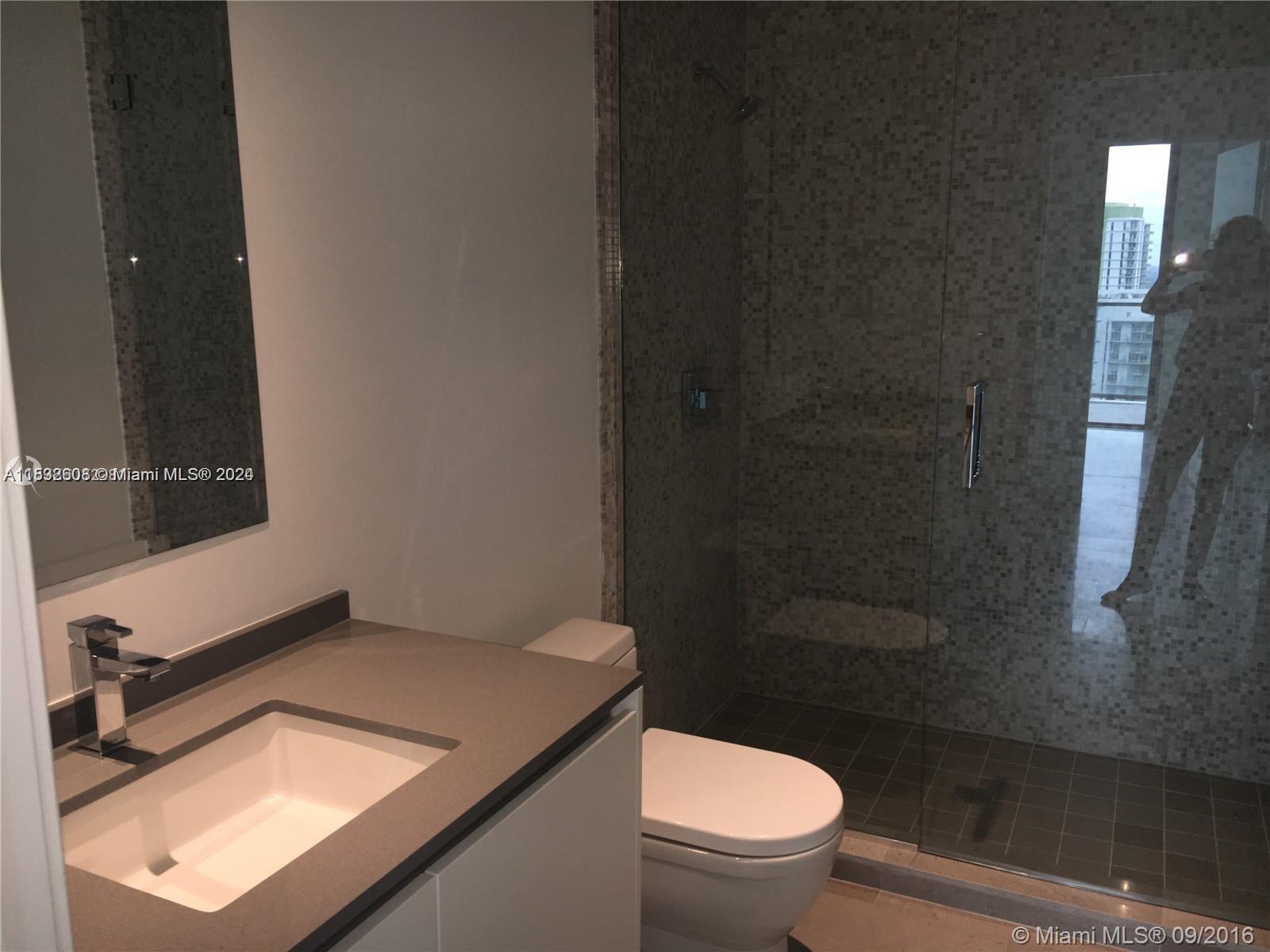 68 Southeast 6th Street, Unit 3510 Miami, FL 33131 - Photo 10 of 20 a bathroom with a granite countertop sink a toilet a mirror and shower