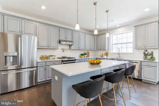 a kitchen with stainless steel appliances granite countertop a sink a stove a refrigerator and island with wooden floor