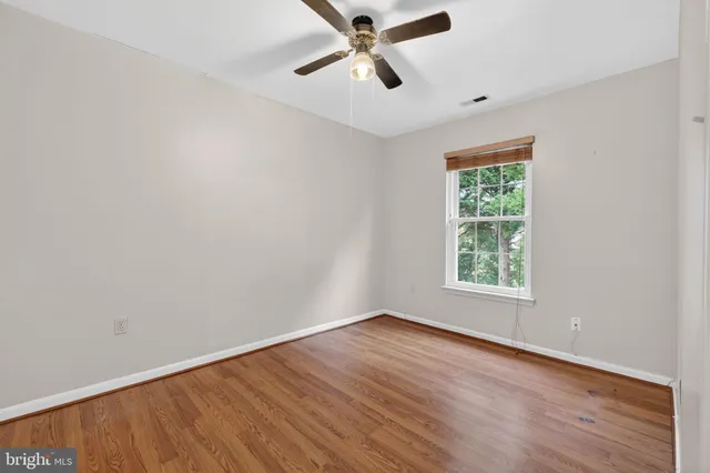 an empty room with wooden floor ceiling fan and windows