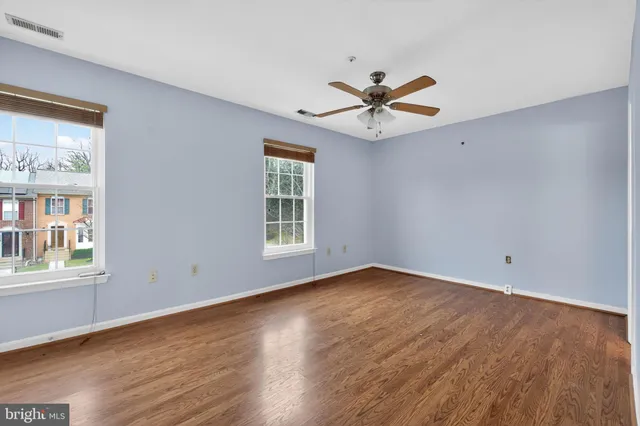 an empty room with wooden floor chandelier fan and windows