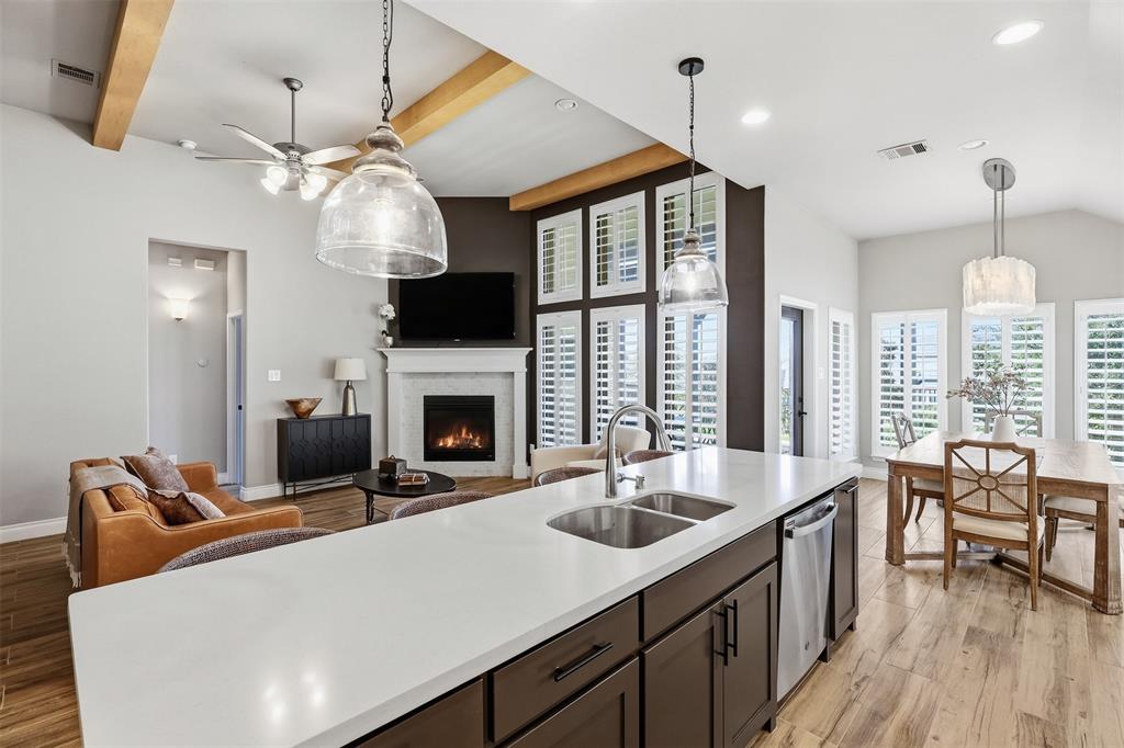 5640 Pradera Road Fort Worth, TX 76126 - Photo 12 of 35 Vaulted ceiling with exposed wood beams, wood-finish flooring, kitchen island with dual sink and stainless steel appliances, corner fireplace with mantel, and multiple windows with plantation shutters