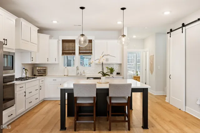 a kitchen with kitchen island a dining table chairs sink and white cabinets