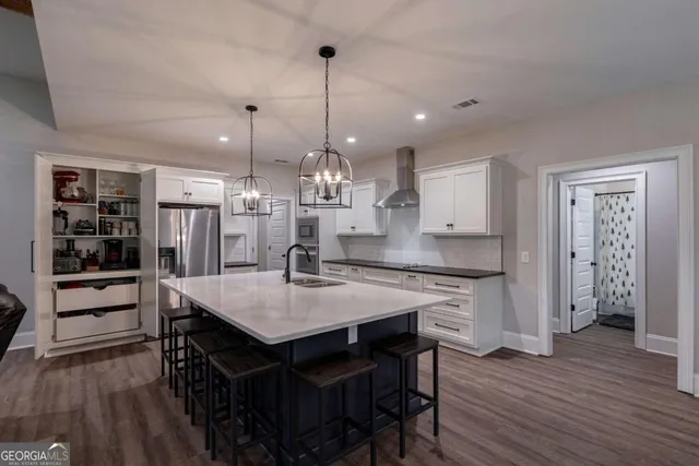 a open kitchen with stainless steel appliances granite countertop a stove a refrigerator a kitchen island a sink dishwasher a dining table and chairs with wooden floor