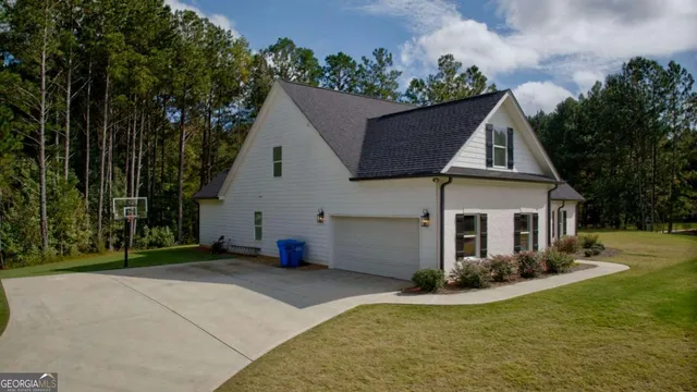 a view of a white house next to a yard with potted plants and large trees