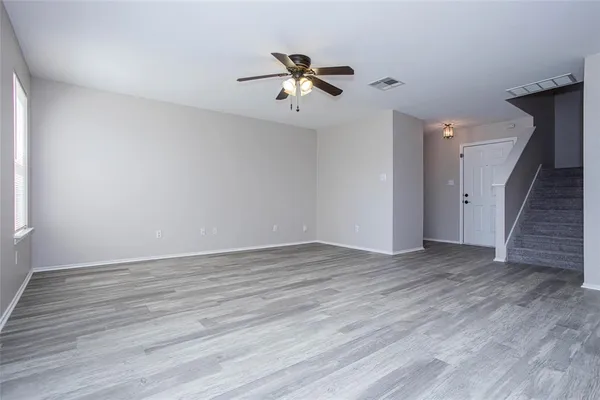 a view of an empty room with wooden floor and a ceiling fan