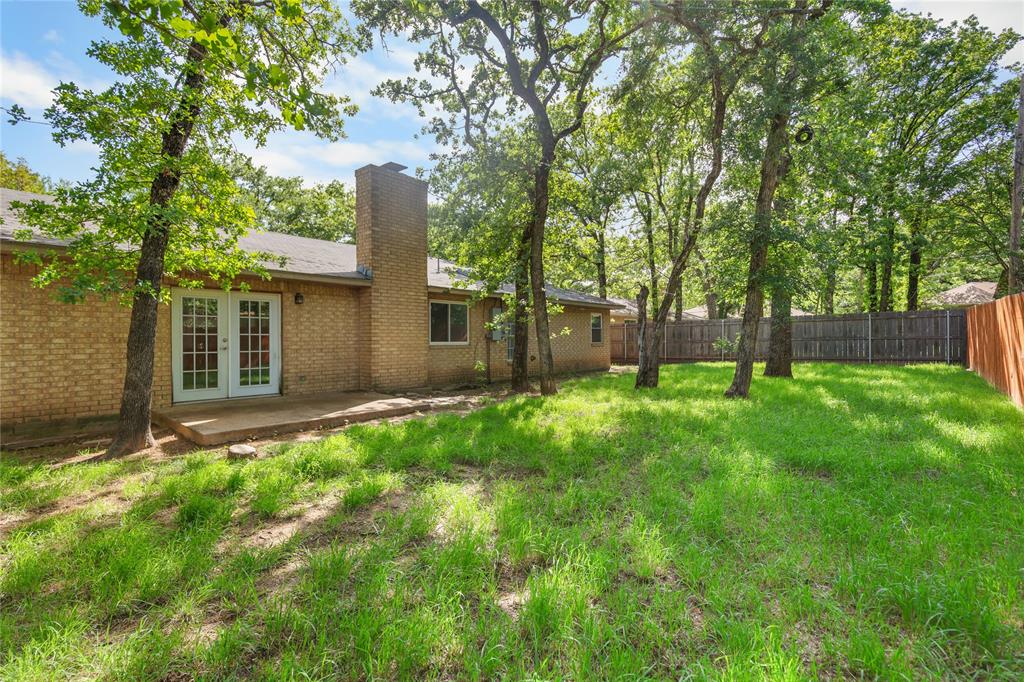 1109 Pine Ridge Drive Azle, TX 76020 - Photo 2 of 24 The property features a brick exterior with a chimney, a patio area, and a yard with mature trees