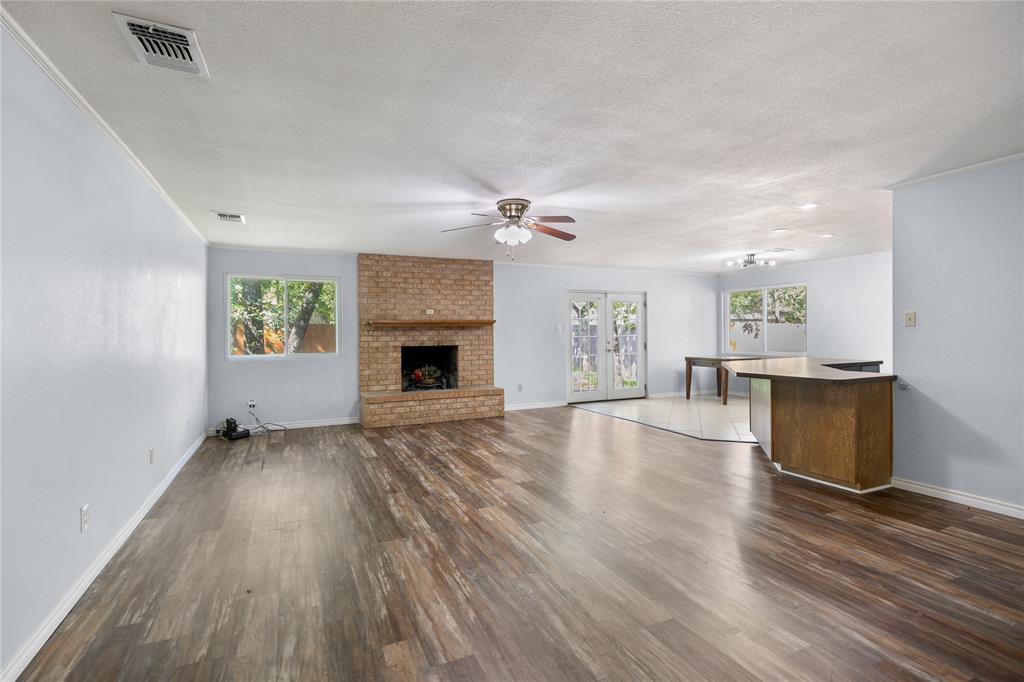 1109 Pine Ridge Drive Azle, TX 76020 - Photo 4 of 24 Spacious living area featuring wood-look flooring, a brick fireplace, and windows providing views of exterior trees
