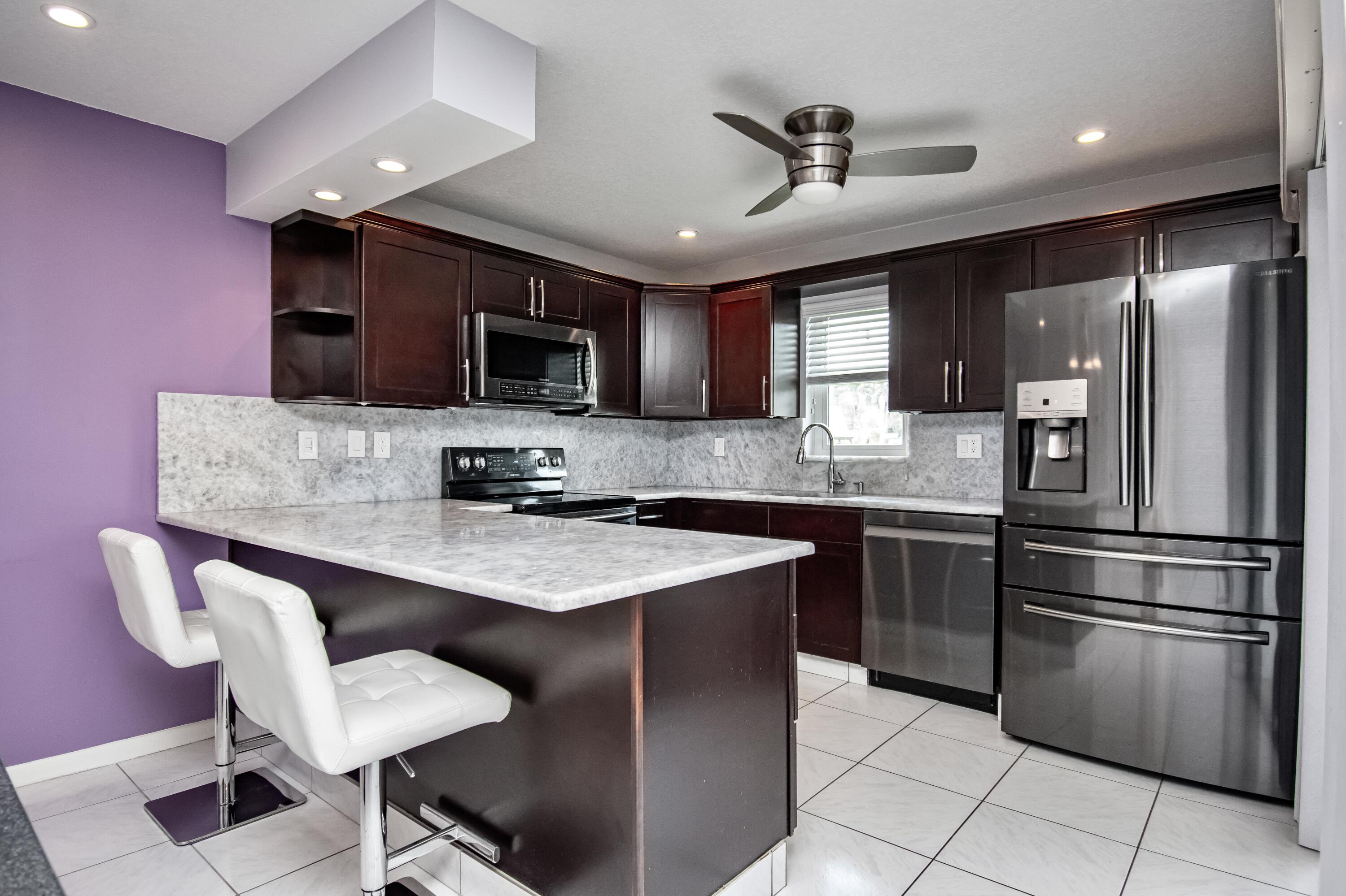 9460 Southwest 61st Way, Unit B Boca Raton, FL 33428 - Photo 5 of 31 a kitchen with stainless steel appliances kitchen island granite countertop a stove a sink dishwasher a refrigerator with a dining table and chairs