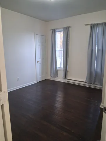 an empty room with wooden floor and windows with curtains