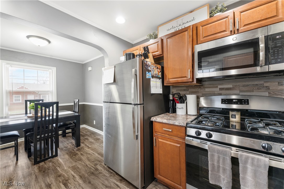 2908 19th Street Northwest Canton, OH 44708 - Photo 19 of 45 Kitchen with crown molding, backsplash, dark wood finished floors, brown cabinetry, and stainless steel appliances