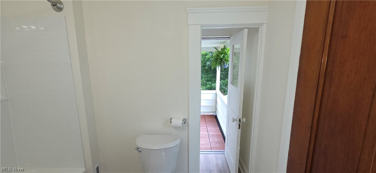 9964 East River Road Elyria, OH 44035 - Photo 29 of 45 White bathroom featuring a toilet, shower, and a doorway opening to an outdoor balcony with wood-finish flooring